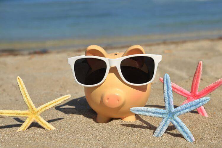 Summer piggy bank with sunglasses on the sand
