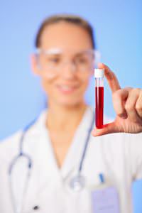 Test tube with blood sample in doctor hand on blue background
