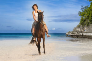 Young Beautiful Woman Riding A Horse On Tropical Beach - How to Avoid Kids While on Vacation in Hawaii