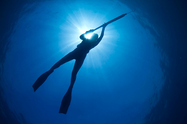 The Definitive Guide to Visiting Hawaii - a silhouette of a young woman spearfishing in hawaii